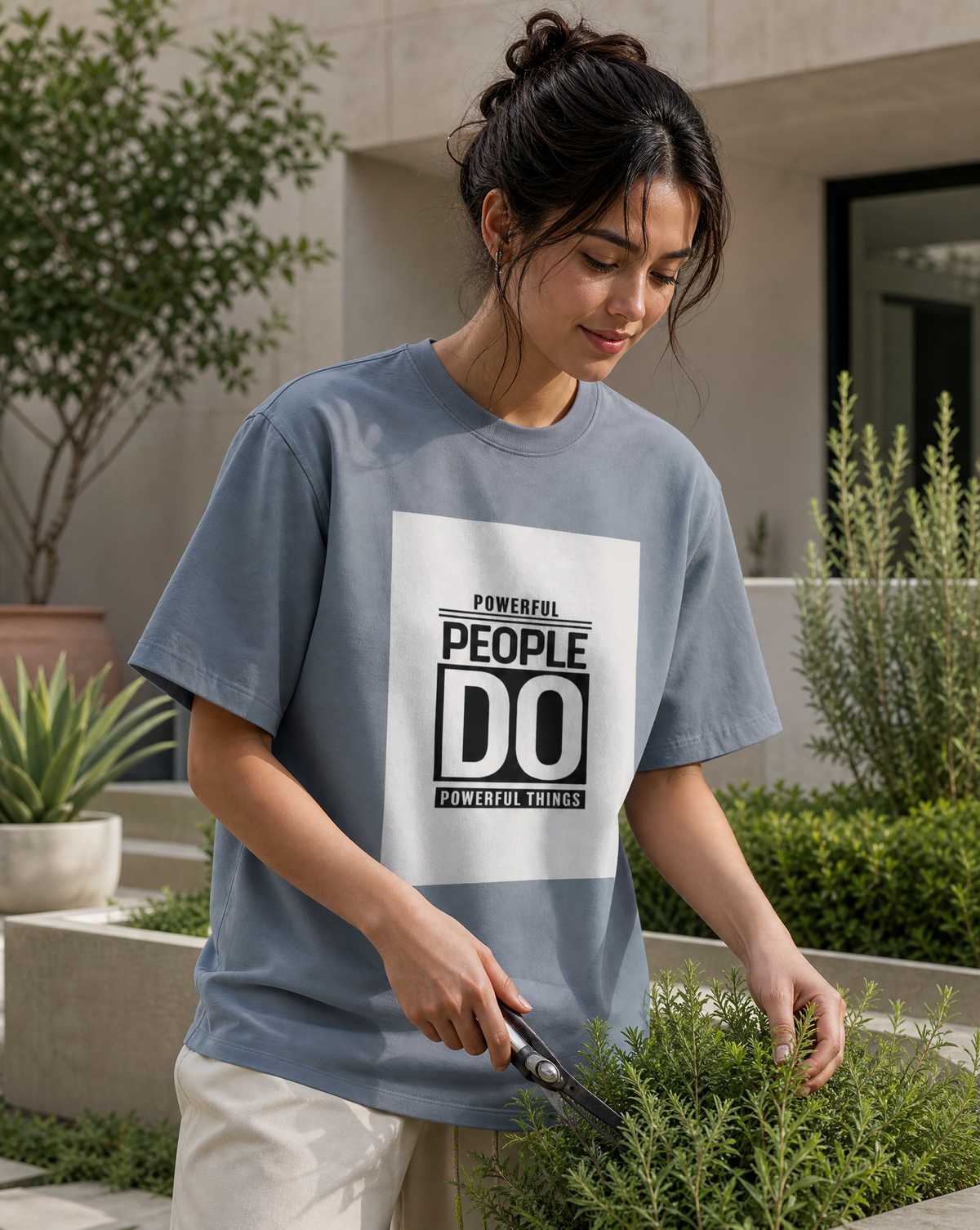 Woman wearing a t-shirt with 'Powerful People Do Powerful Things' text, trimming plants outdoors.