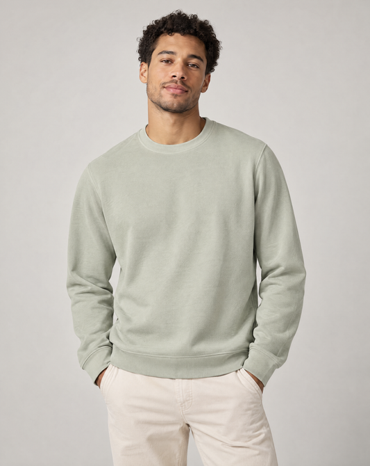 A man wearing a light sage green crewneck sweatshirt and cream pants.